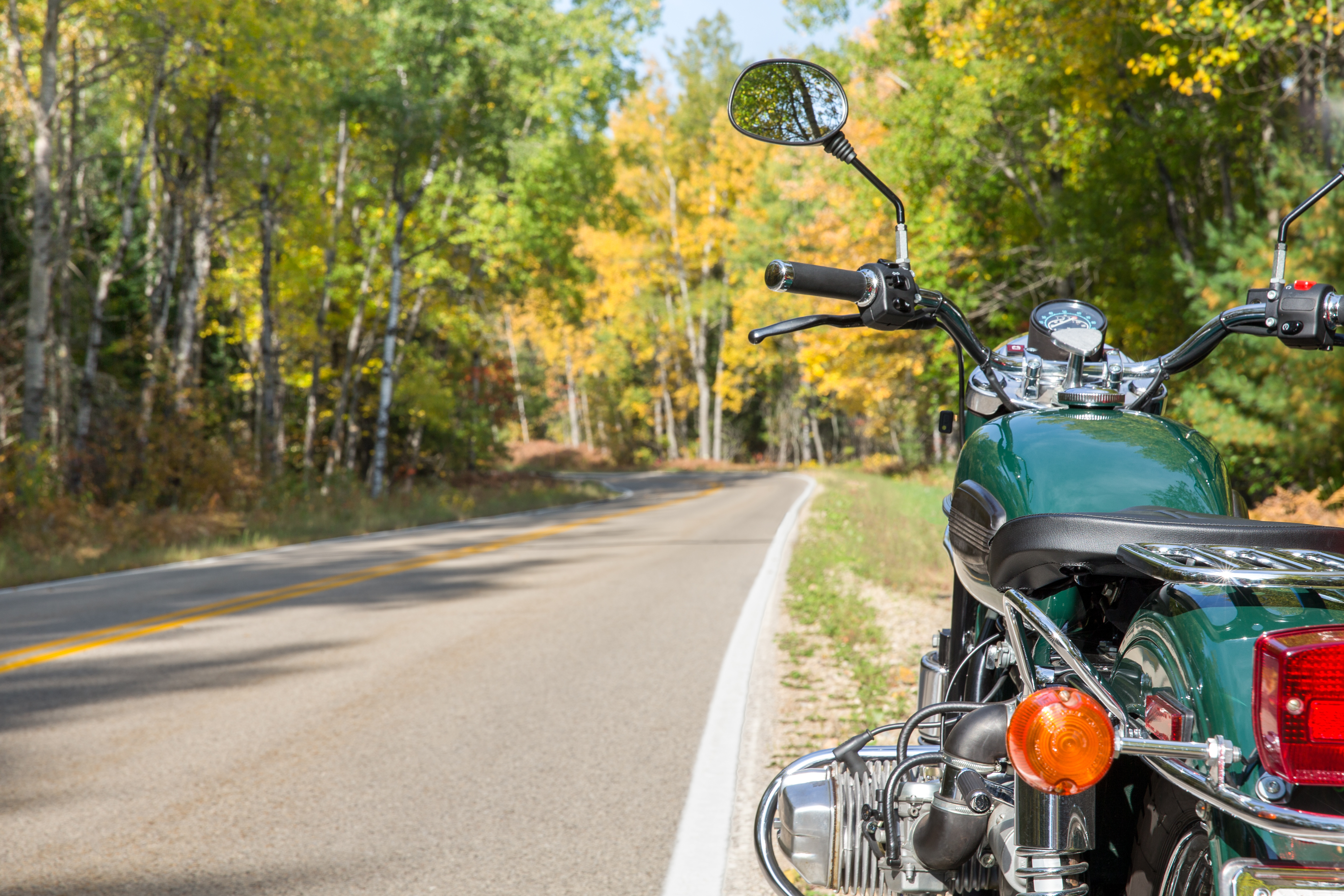 A green motorcycle alongside a curving open road in the Fall.  Selective focus on motorcycle with copy space in left frame if needed.  Ready for adventure.
