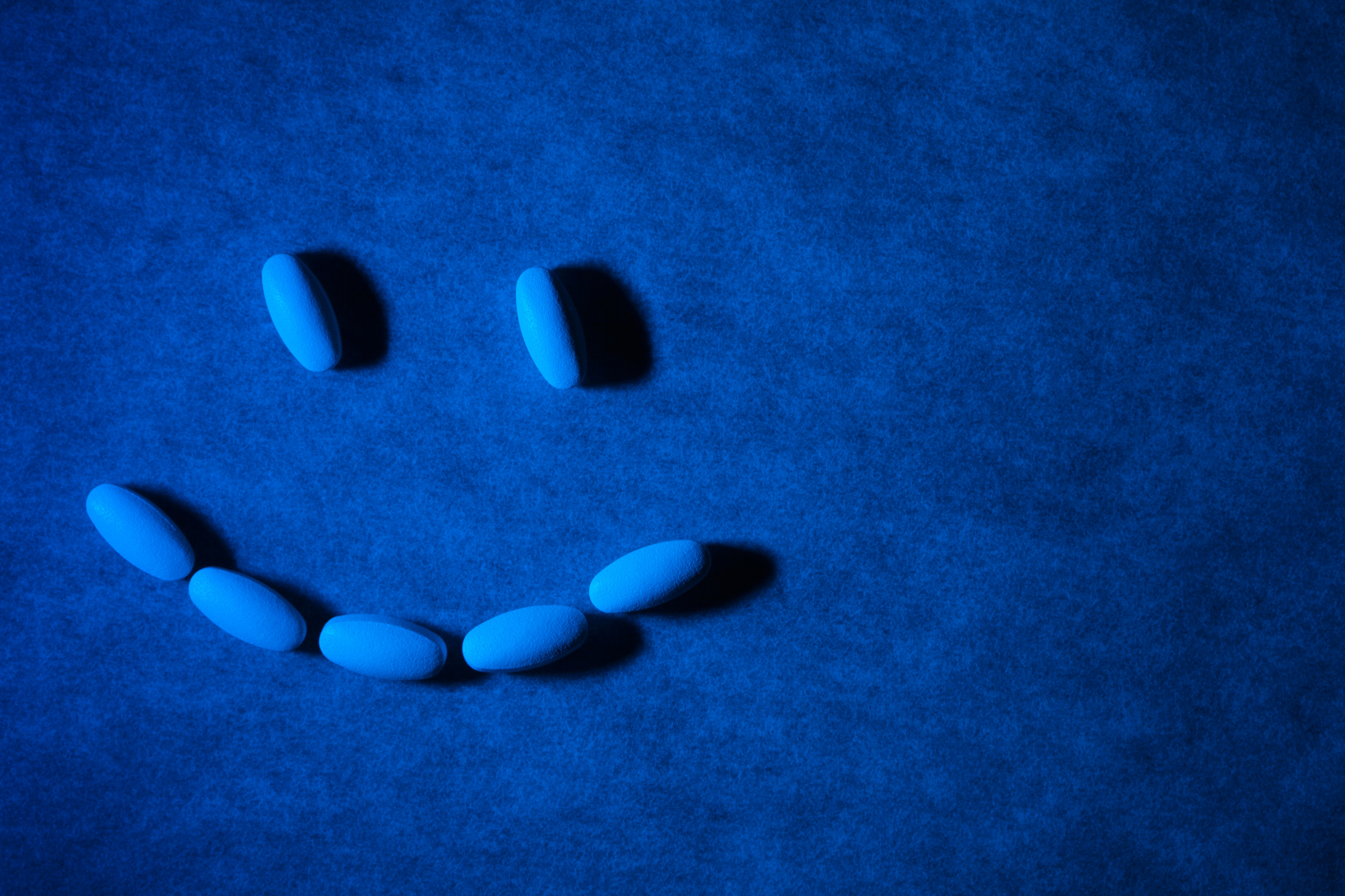 Medical pills on textured background with blue lighting. Pills are arranged in the form of a smiling face.