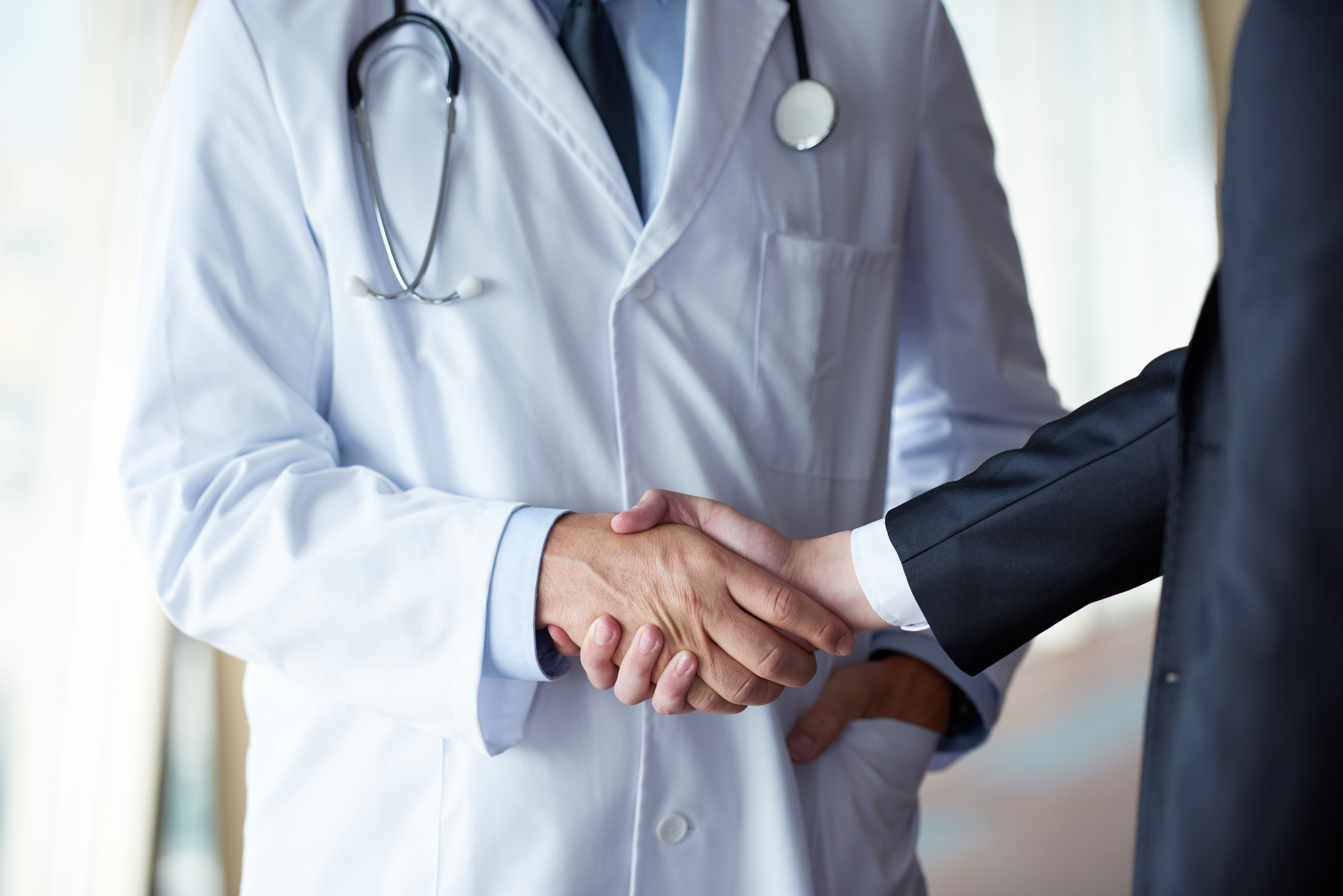 doctor handshake with a patient at doctors bright modern office in hospital