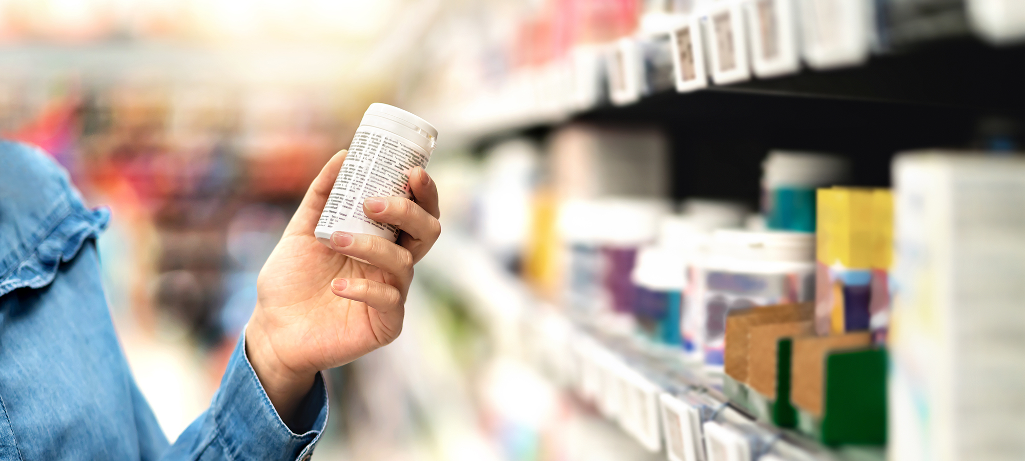 Customer in pharmacy holding medicine bottle. Woman reading the label text about medical information or side effects in drug store. Patient shopping pills for migraine or flu. Vitamin or zinc tablets.