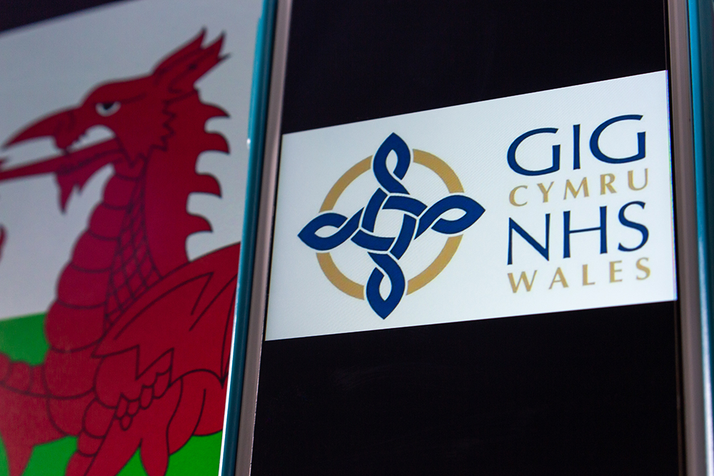 Kumamoto, JAPAN - Sep 6 2021 : Closeup logo of NHS Wales (Welsh: GIG Cymru), the publicly funded healthcare system in Wales, on iPhone on Welsh flag. It’s the one of the National Health Services in UK