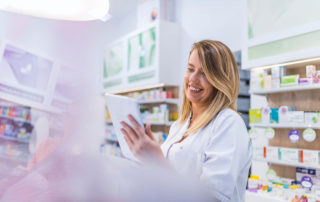 Pharmacist working with a tablet computer in the pharmacy holding it in her hand while reading information. Cheerful happy pharmacist chemist woman working in pharmacy drugstore with tablet computer