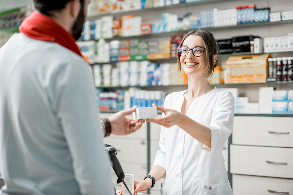Young woman pharmacist giving medications to the male client standing at the paydesk of the pharmacy store
